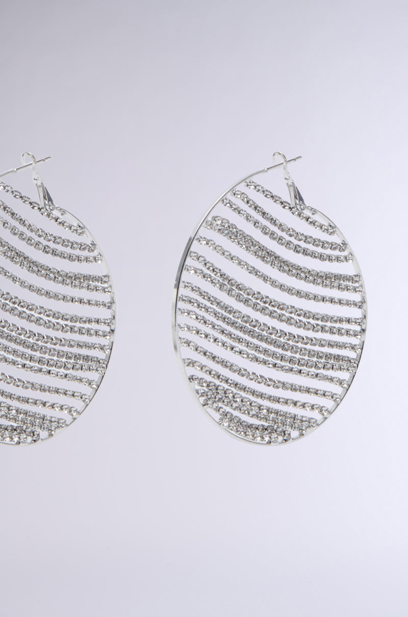 The MAIN MOMENT BLING HOOP EARRINGS feature a large design with alternating patterns of sparkling silver lines and clear rhinestones, all set against a sleek metallic base.