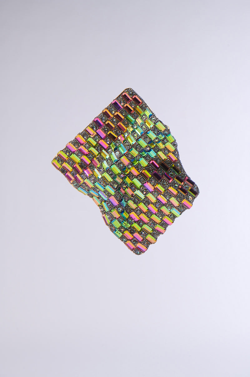 The SHINE BRIGHT EARRING is a colorful, woven, three-dimensional accessory with a wavy grid pattern and high-shine finish in vibrant yellow, pink, green, and orange tones, displayed against a plain light gray background. 3