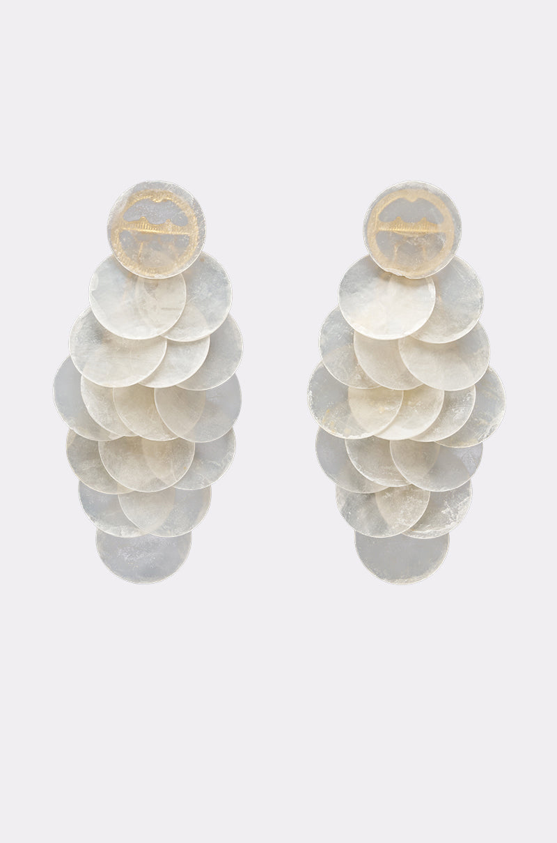 The GIMME MY SHELLS EARRING features multiple overlapping translucent white discs, reminiscent of mother-of-pearl, dangling below a gold engraved stud. Set against a light gray background. 1