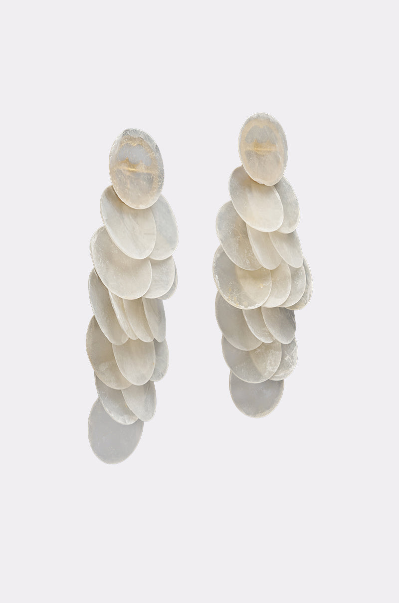 The GIMME MY SHELLS EARRING features layered, overlapping translucent white discs arranged in a cascading design for an elegant statement look against a plain light background. 2
