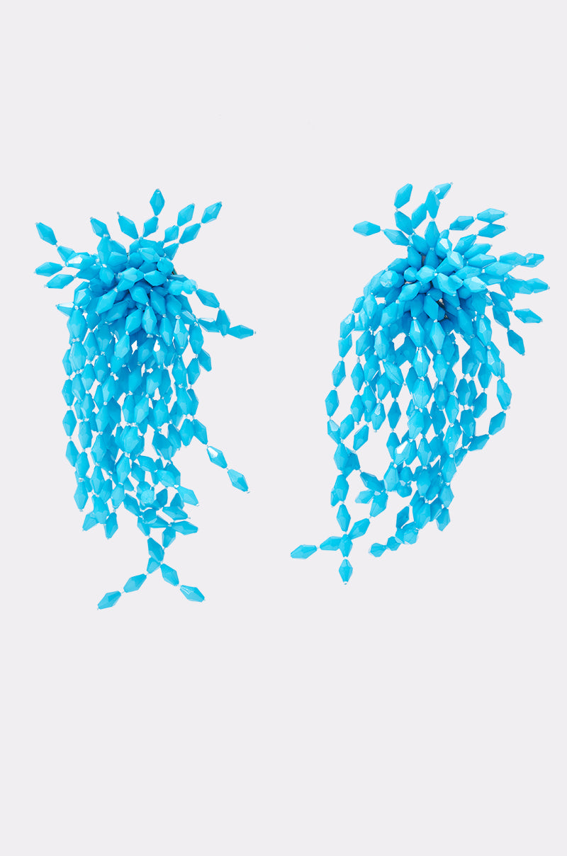 The TO THE SEA EARRING features vibrant turquoise with cascading strands of small, angular beads for a bold festival look, shown against a plain white background.