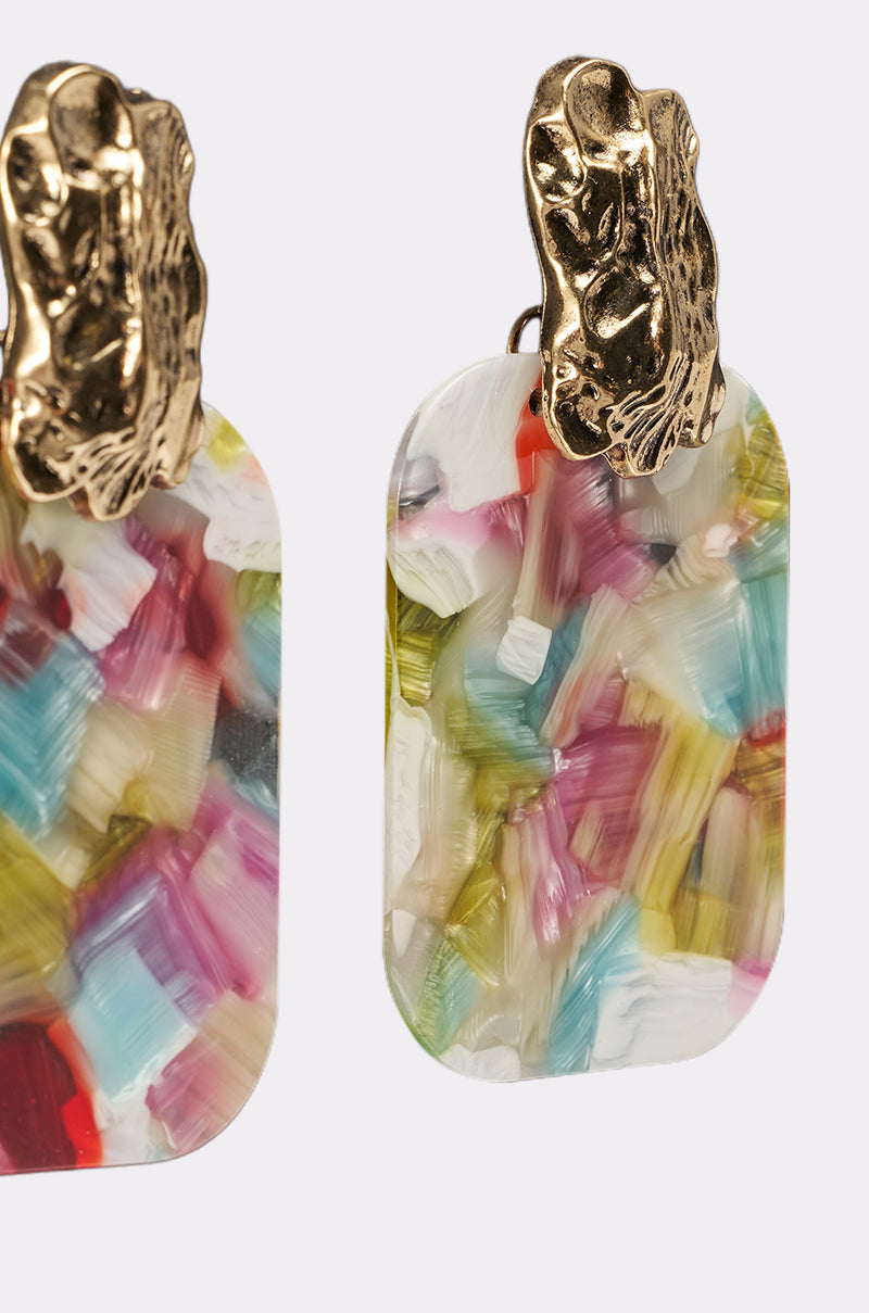 Close-up of AT A RESORT EARRING: multicolor drop earrings in pink, blue, yellow, and white with a marbled pattern, topped with irregular hammered gold-tone accents. Shown against a plain light background. 3