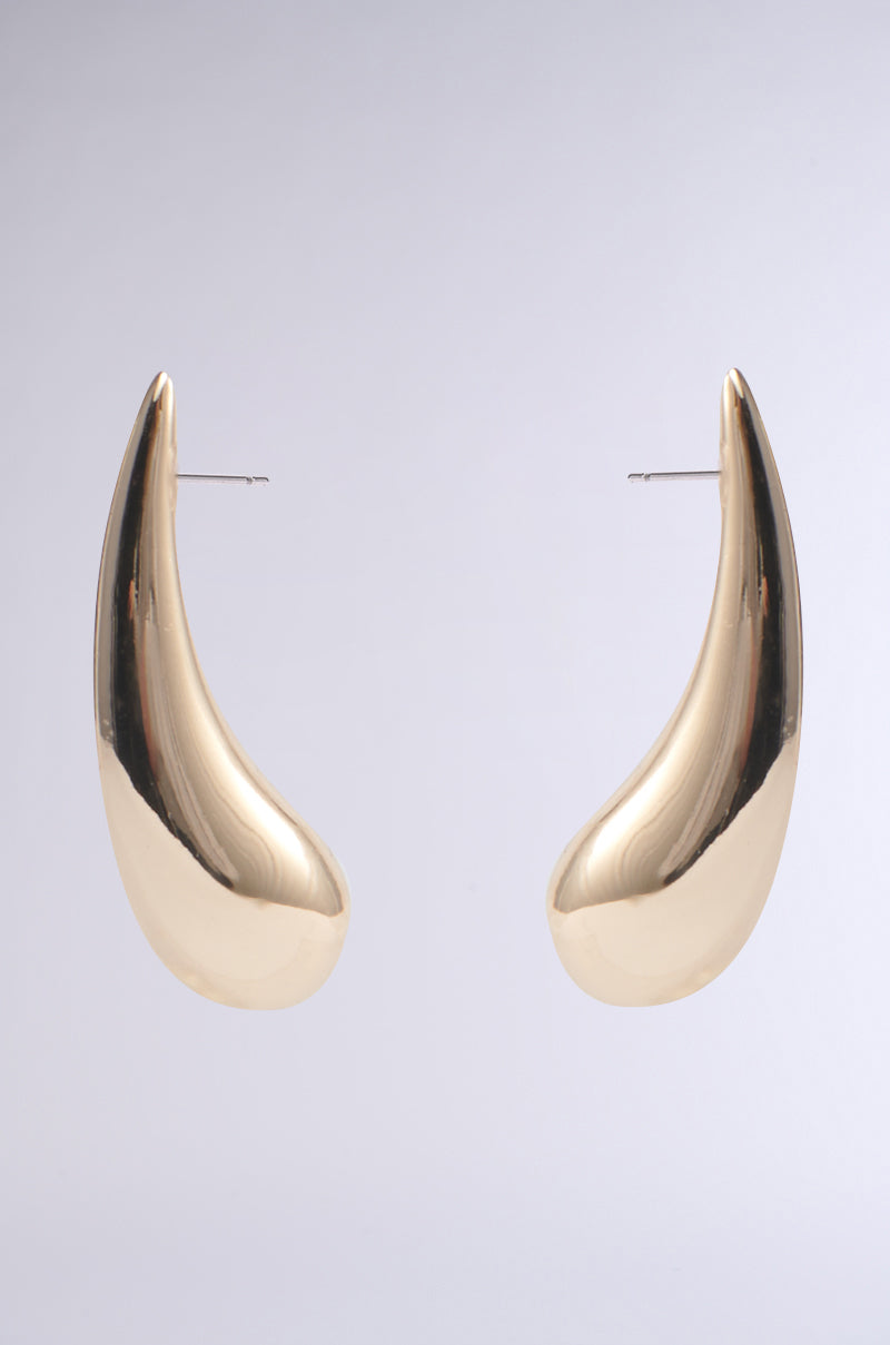 IN THE WIND EARRING: Large, gold, crescent-shaped earrings with a smooth, reflective finish shown against a plain, light grey background.