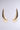 IN THE WIND EARRING: Large, gold, crescent-shaped earrings with a smooth, reflective finish shown against a plain, light grey background.