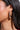 Close-up of a woman's ear wearing the IN THE WIND EARRING, a large abstract gold silhouette, paired with a small silver hoop. Her dark hair is tucked behind her ear and her skin glows in natural light.