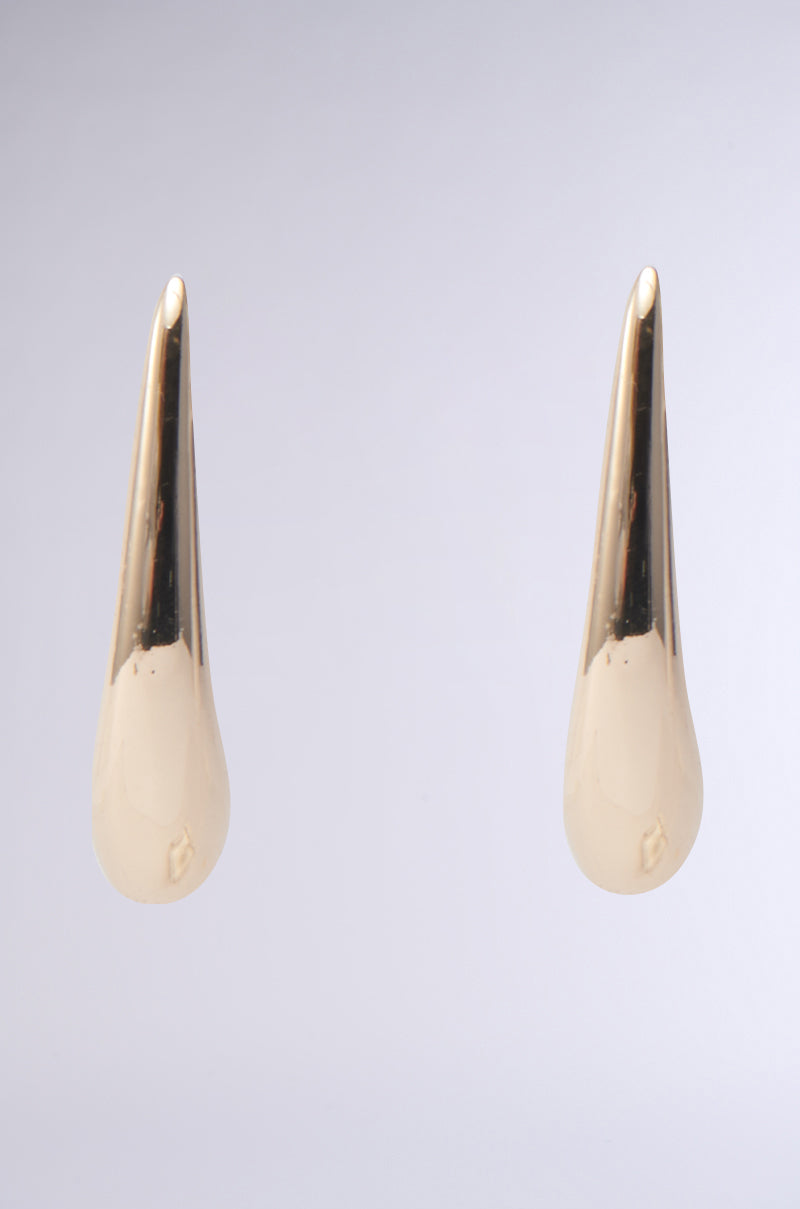 The IN THE WIND EARRING, with its gold-tone finish and smooth, shiny surface, is displayed against a plain light gray background, emphasizing the elegant, abstract teardrop silhouette.