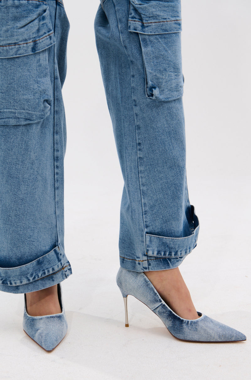 A person stands on a white surface wearing loose, light blue acid wash denim cargo pants with rolled cuffs and the AZALEA WANG KEATON DENIM STILETTO PUMP.