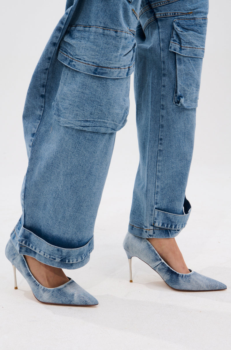 A person in loose-fitting blue acid wash denim cargo pants and AZALEA WANG KEATON DENIM STILETTO PUMPS stands on a white surface, blending casual and formal styles.