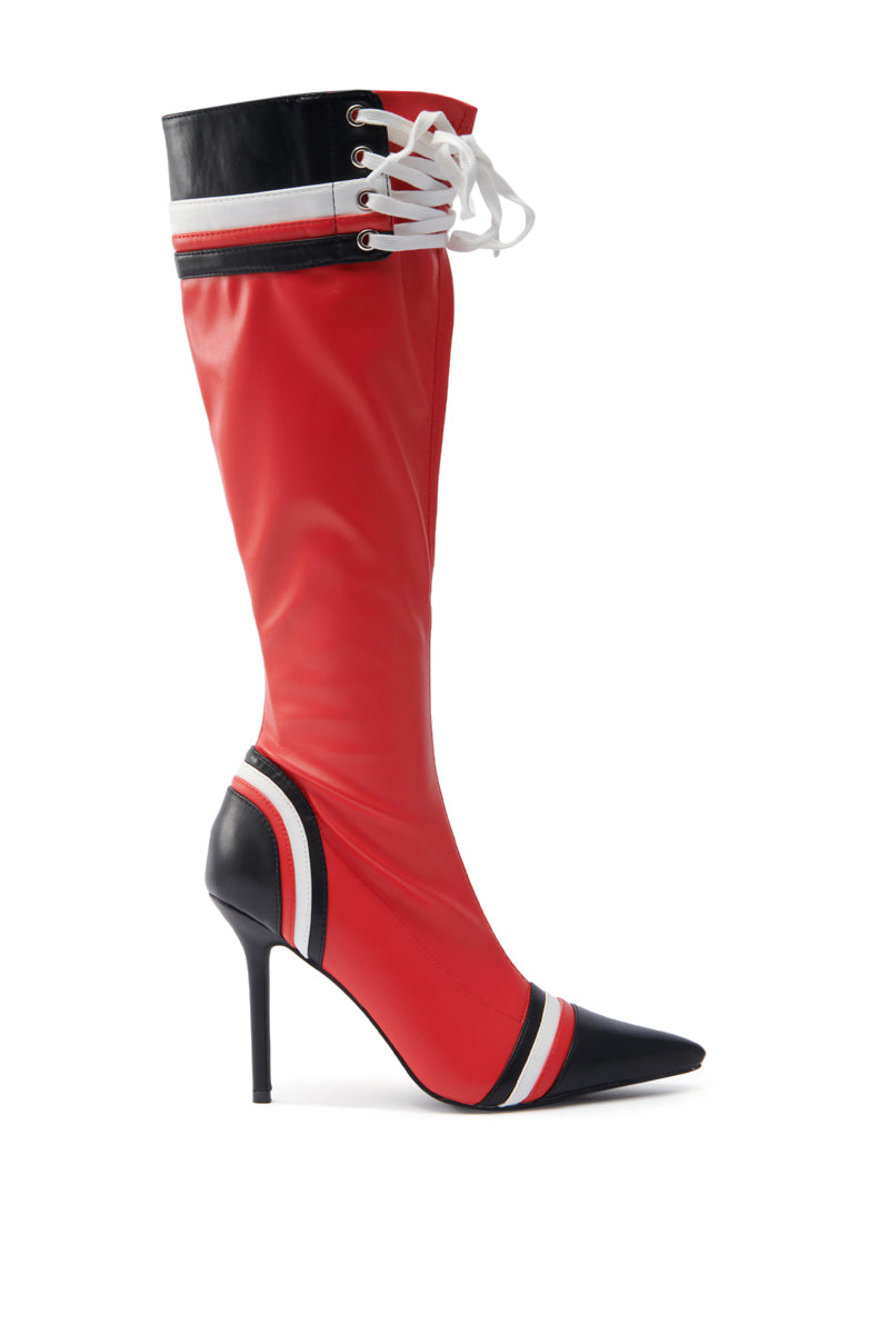The AZALEA WANG KELCIE RED STILETTO BOOT is a red knee-high boot made from faux leather, featuring black and white details. It has a pointed toe, red stiletto heel, and elegant white laces near the top.