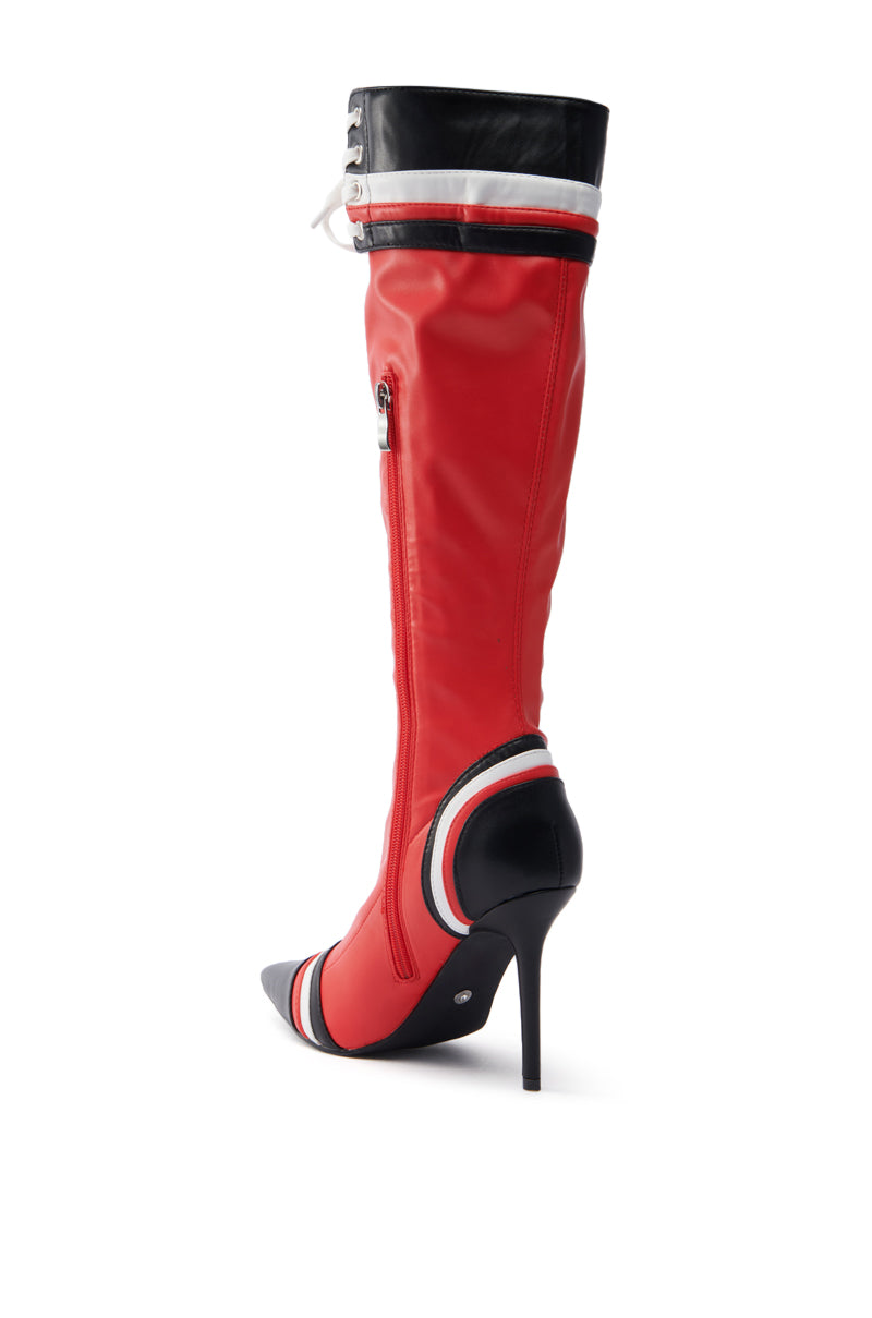 The AZALEA WANG KELCIE RED STILETTO BOOT features a red faux leather knee-high design with a pointed toe, black and white accents, a side zipper, and horizontal stripes at the top and heel. The boot's tall stiletto heel adds style and sophistication.