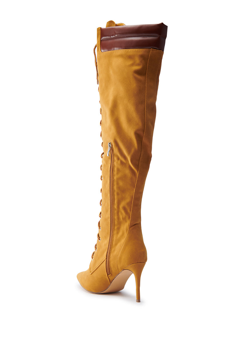 The KENDRIX SUEDE KNEE-HIGH BOOT is a tan faux suede boot with a pointed toe and sleek stiletto heel. It features a lace-up front, side zipper, and brown leather trim at the top.