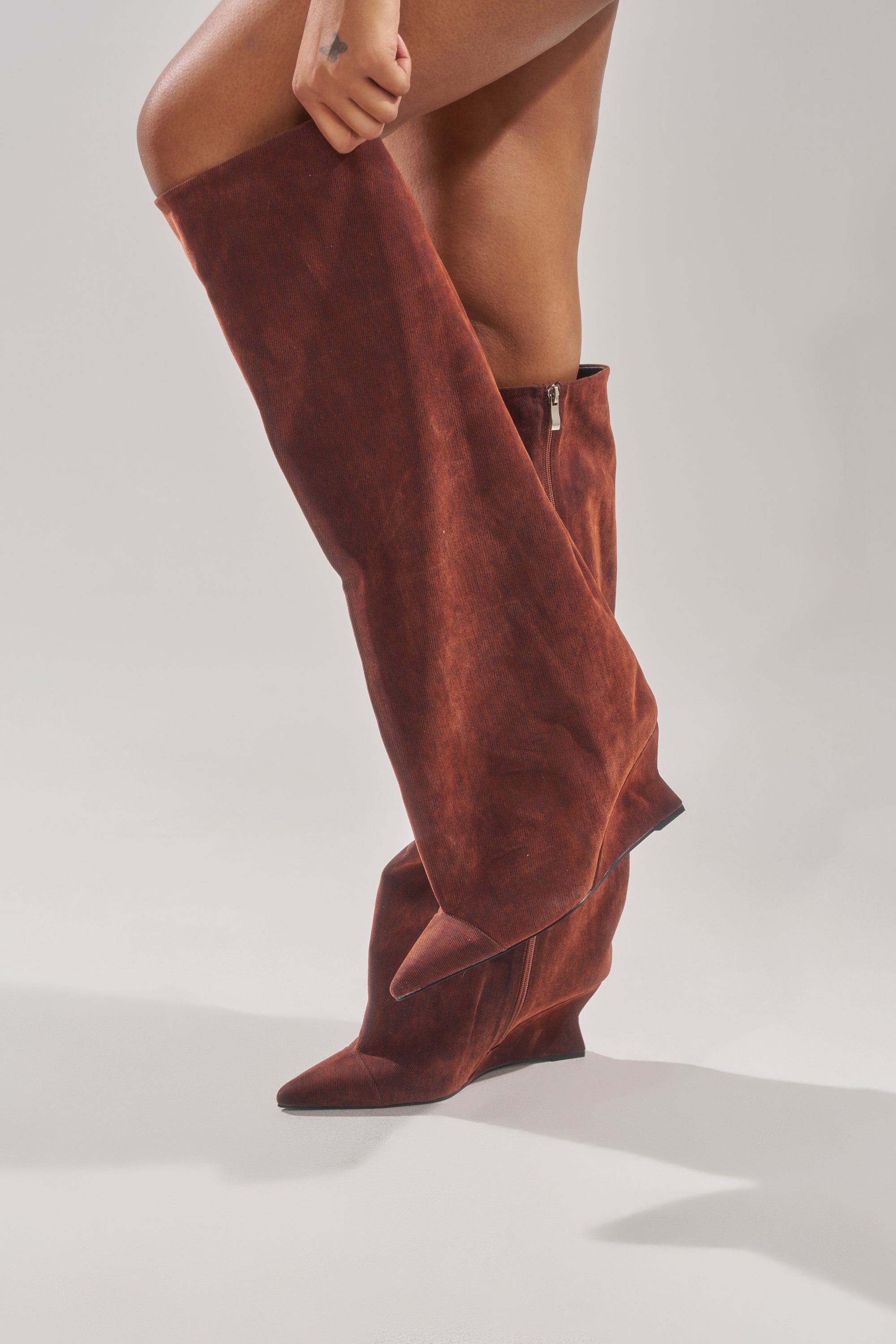 A person is wearing AZALEA WANG KENYA BURNT ORANGE VELVET KNEE HIGH WEDGE BOOTS with pointed toes and a side zipper, standing against a plain light background. Only the legs and part of one hand are visible.