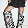 A person models the AZALEA WANG KENYA ZEBRA KNEE HIGH WEDGE BOOT with a black graphic t-shirt dress, standing against a plain white wall. Only the lower half of their body is shown.