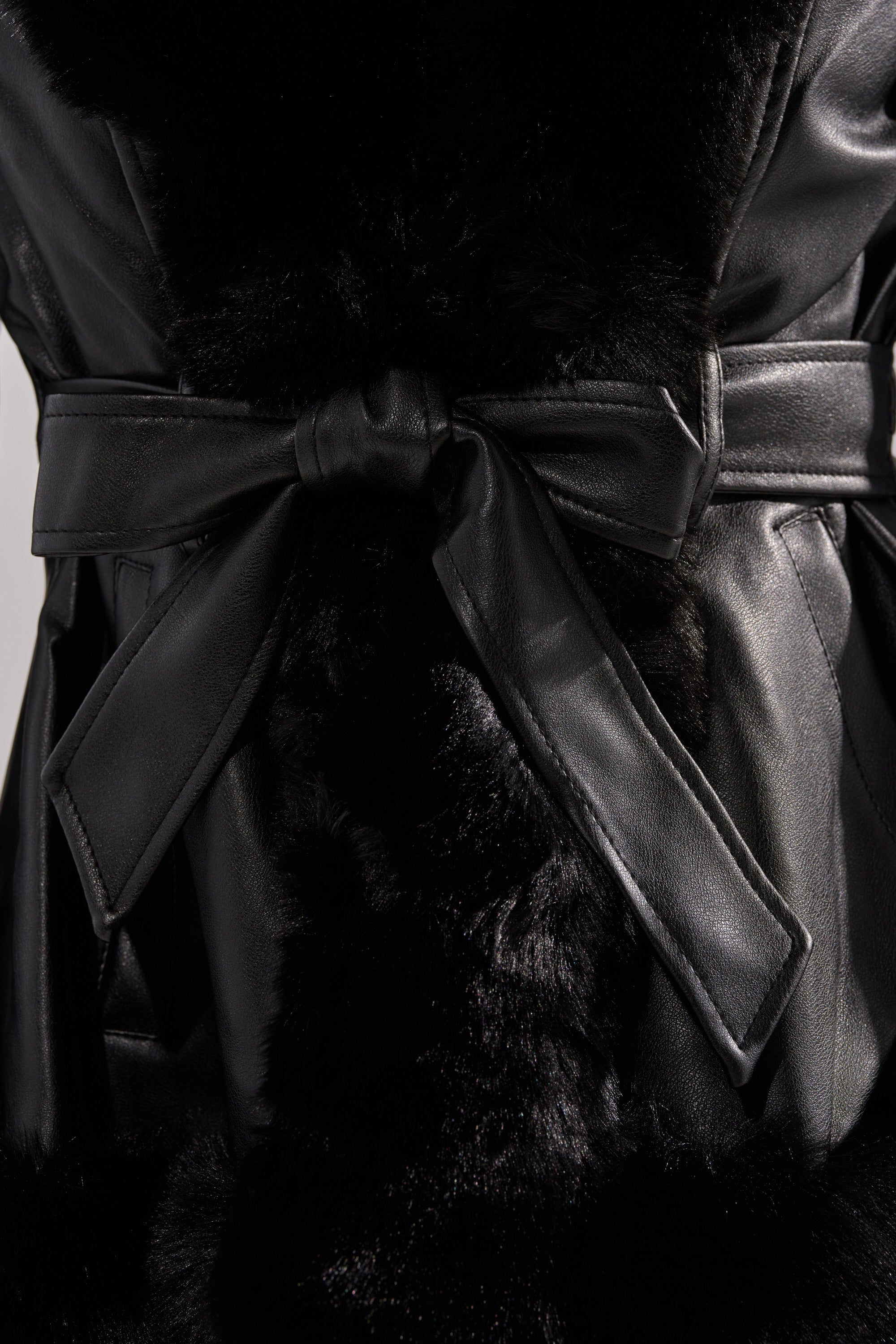 A close-up of the KENZY FUR TRIM PEPLUM MOTO IN BLACK shows a black leather jacket with a bow-tied waist belt and soft plush fur trim running down the center.