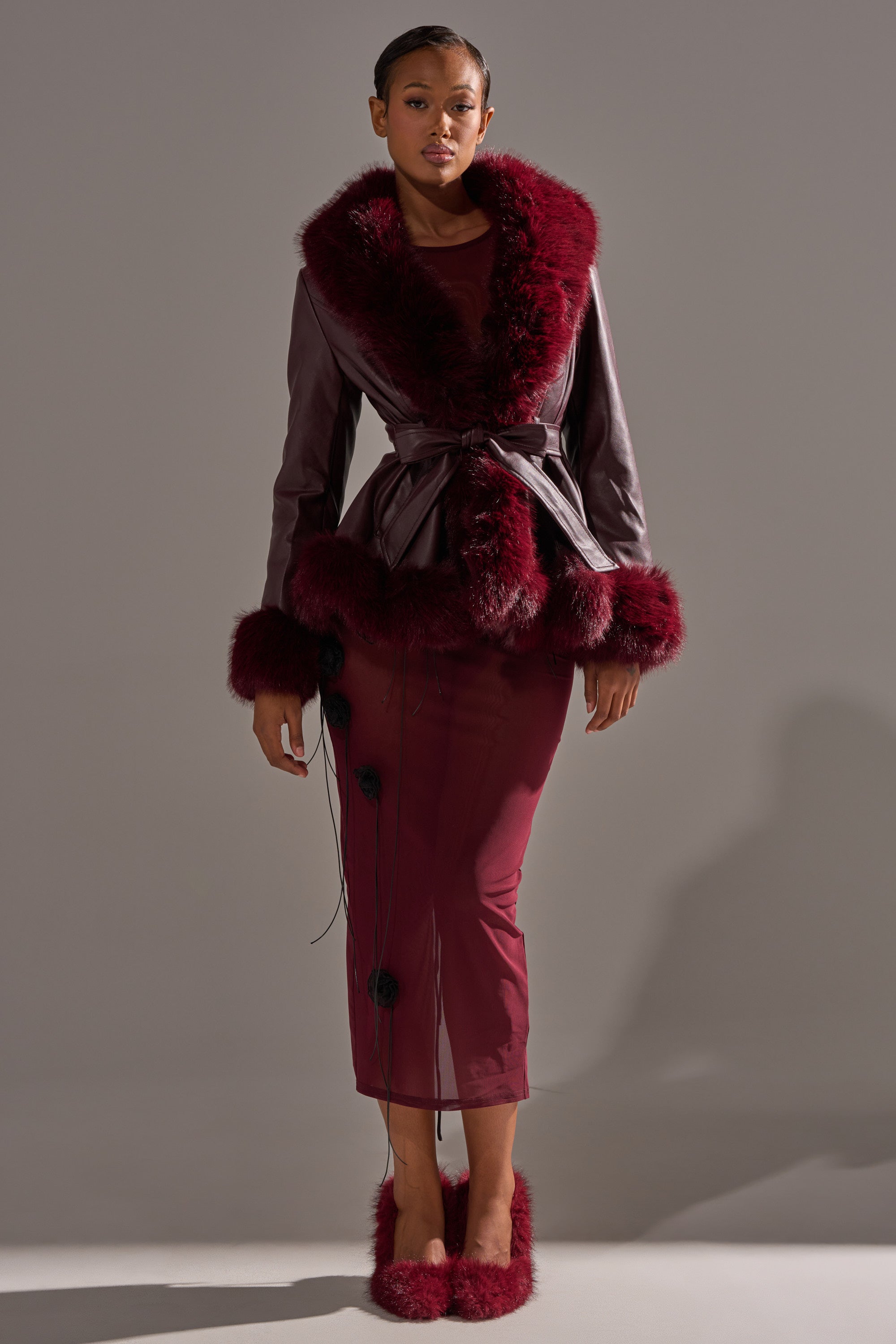 A woman models the KENZY FUR TRIM MOTO IN BURGUNDY, styled with a matching fitted skirt and fuzzy burgundy shoes, set against a neutral background. 6