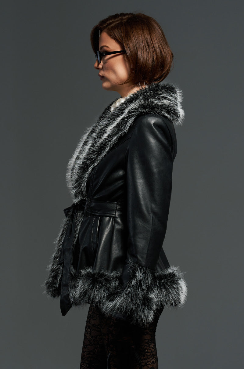 A woman with short brown hair and glasses is wearing the sleek NEW KENZY FUR TRIM MOTO jacket over patterned leggings. She stands in profile against a gray background.