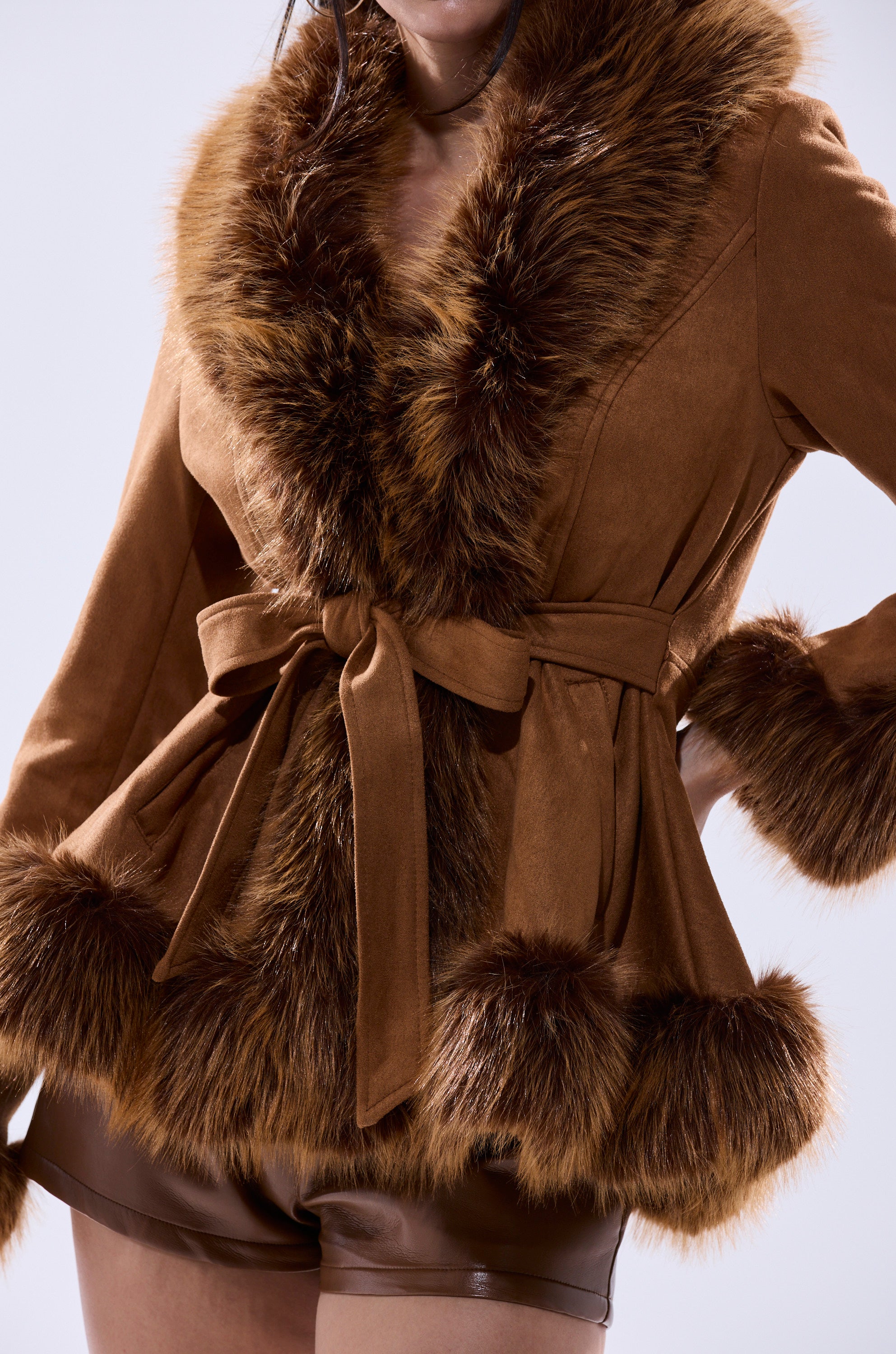 Model wearing the SUEDE KENZY FUR TRIM MOTO—a vintage-inspired faux suede jacket with fur trim and a tied waist—paired with matching brown shorts, photographed from shoulders to mid-thigh against a light background.