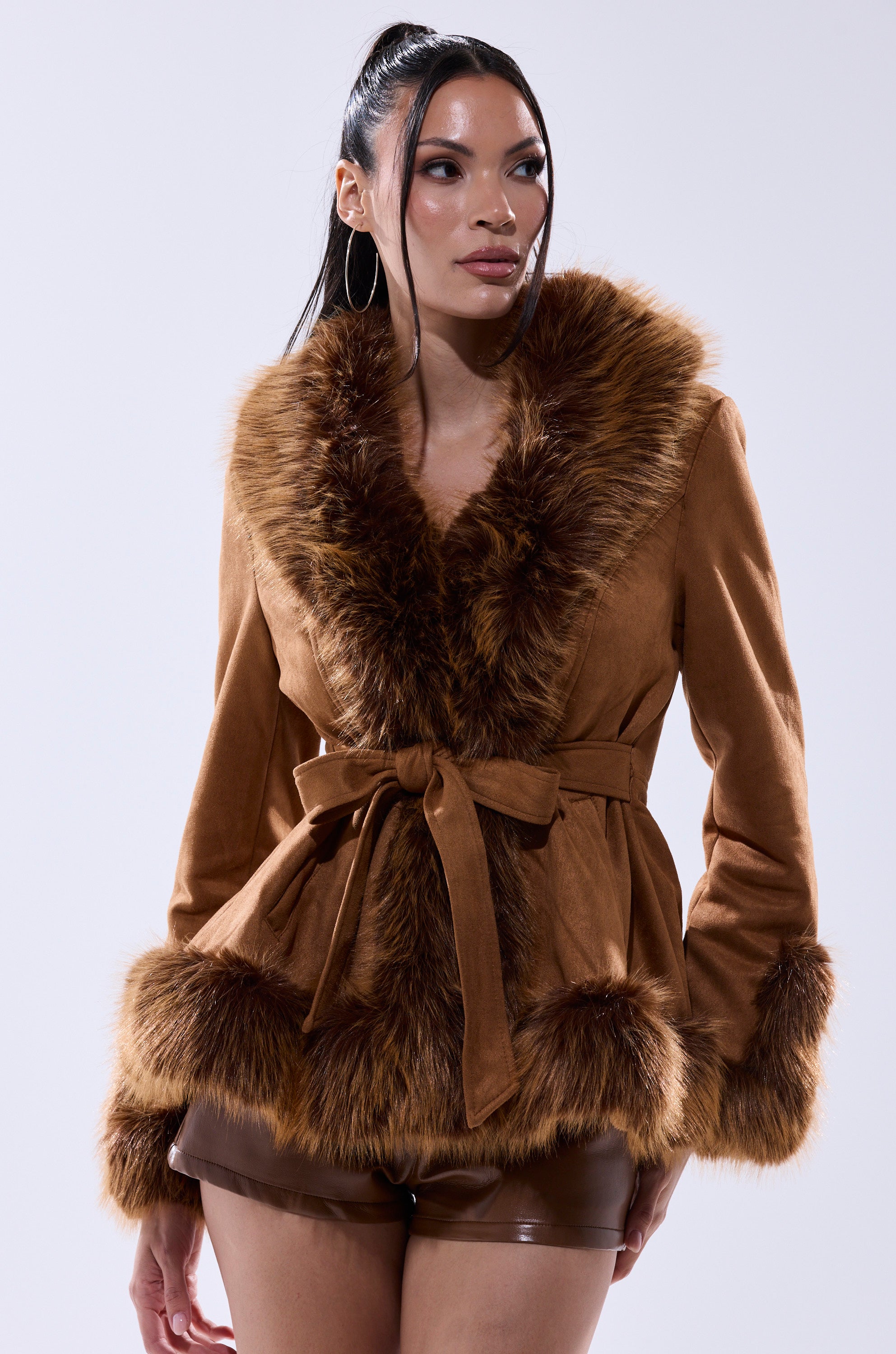 A woman models the SUEDE KENZY FUR TRIM MOTO, a vintage-inspired faux suede jacket with fur trim and belted waist, paired with matching brown shorts against a plain light background.
