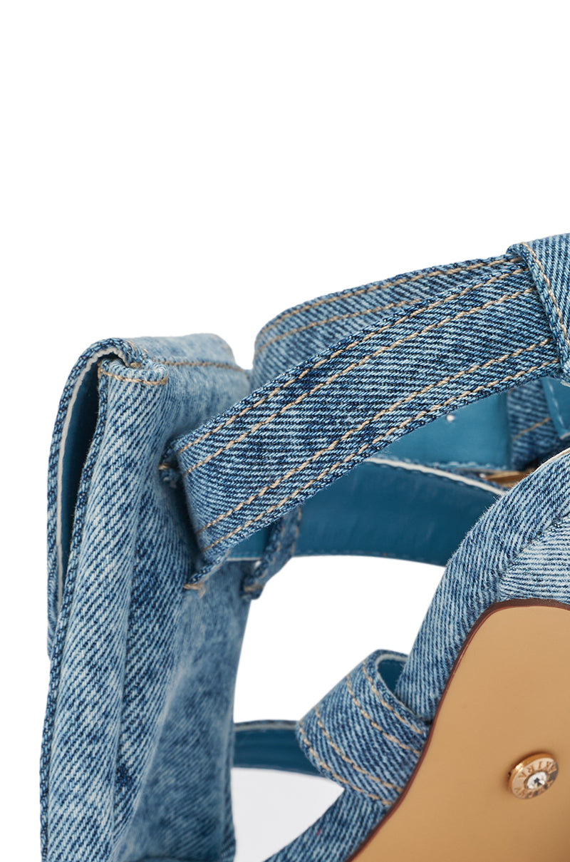 Close-up of the AKIRA GOLD KERSHAW DENIM POCKET STILETTO STRAP SANDAL, featuring blue denim with visible stitching, a Velcro strap, tan sole, and textured material for a modern twist on classic square toe heels. 9