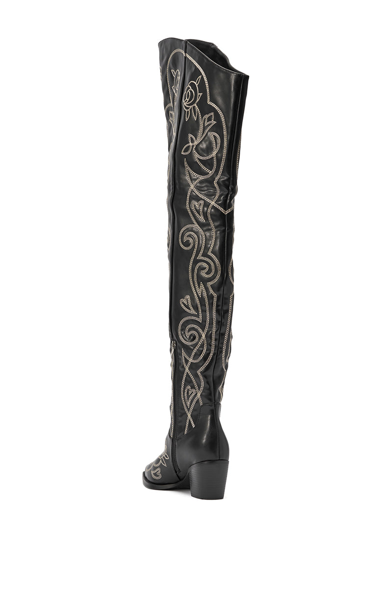 The AZALEA WANG KESS BLACK WESTERN THIGH HIGH CHUNKY BOOT is a black faux leather, over-the-knee style featuring low chunky heels and eye-catching white embroidered floral and swirl patterns for bold western flair. 7