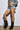 A person poses against a plain backdrop in a two-piece houndstooth outfit with a cropped top and frilled-edge shorts, paired with the AZALEA WANG ELLIS BLACK BOOTIE, featuring pointed toes to emphasize the ensemble's design and fit.