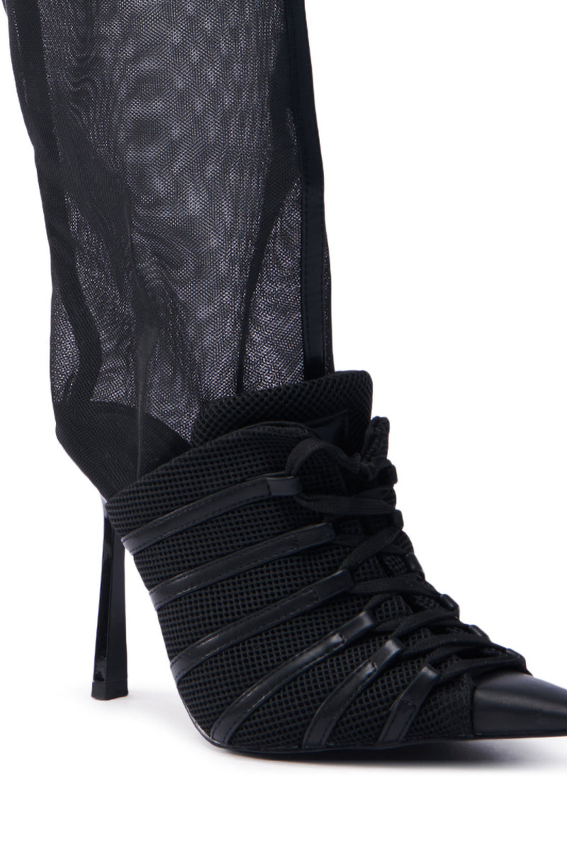The AZALEA WANG ELLIS BLACK BOOTIE features intricate strap detailing and a mesh upper in a close-up, showcasing its pointed toe with a sleek, slender stiletto heel.