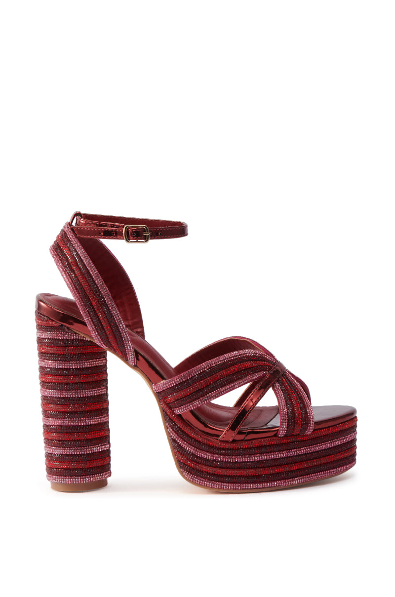 The AZALEA WANG KINSLEE BURGUNDY MULTI CHUNKY SANDAL features a red, shimmery textured finish, chunky platform heel, ankle buckle strap, crisscross toe straps, and sparkling rhinestone accents.