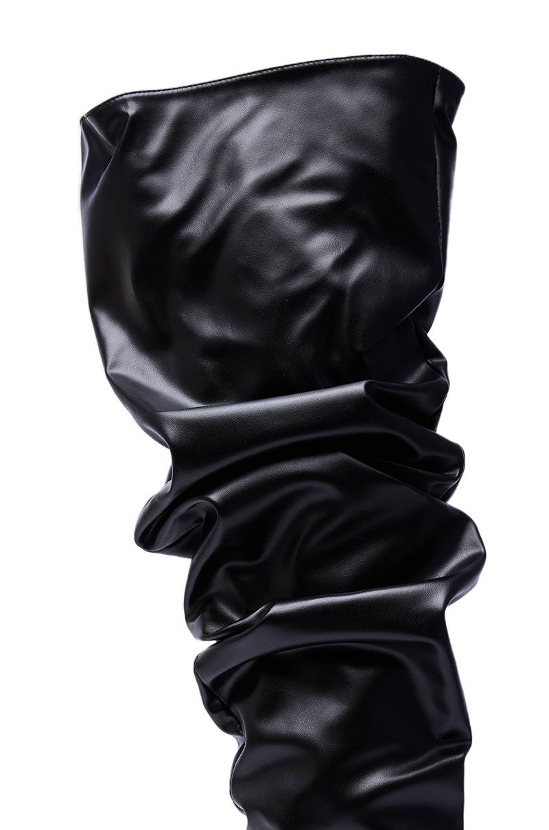 A close-up of the AZALEA WANG KIPLING BLACK RUCHED UP FLAT BOOT shows its shiny faux leather, thigh-high fit, and slouchy ruched texture against a white background.