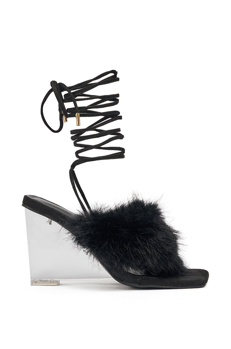 The AKIRA GOLD KIRI BLACK FUR THONG SANDAL WITH CLEAR HEEL features black faux fur on the toe strap, a transparent PVC wedge heel, and long black lace-up ankle straps with gold tips. 3
