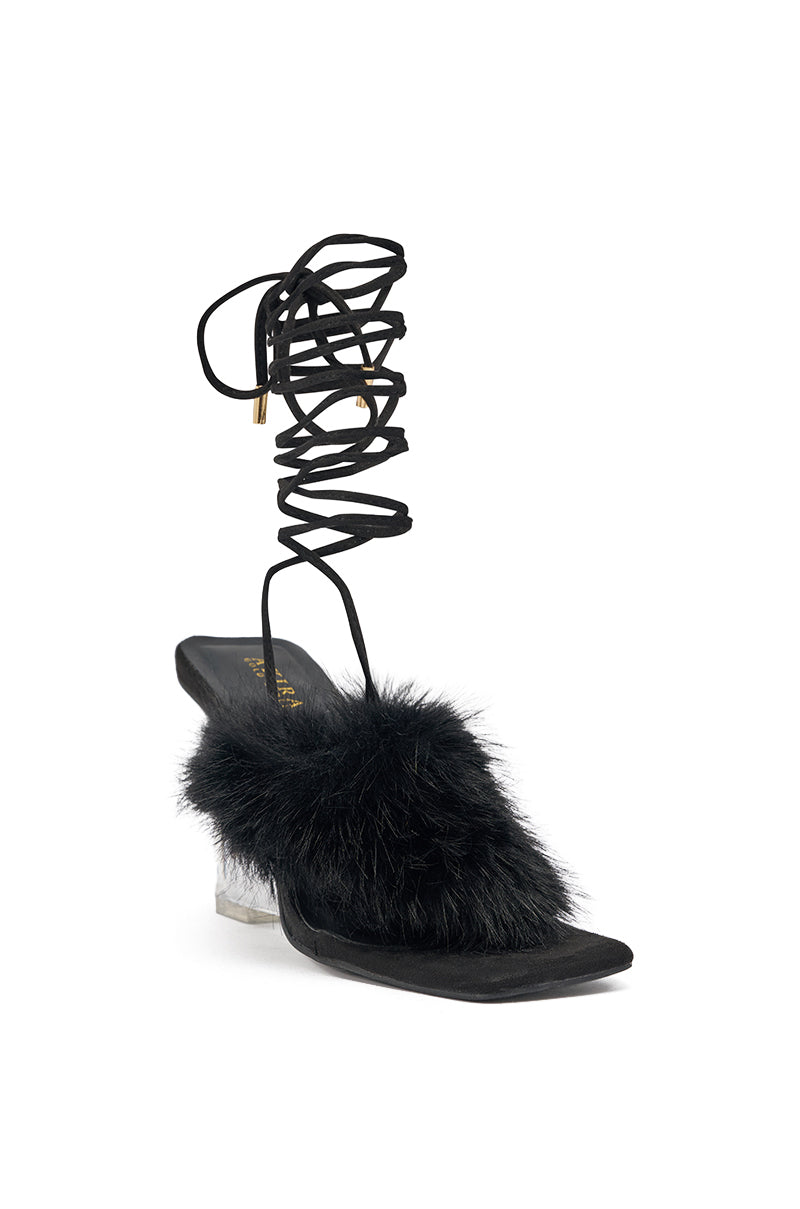 The AKIRA GOLD KIRI BLACK FUR THONG SANDAL features a black square toe, fluffy faux fur front strap, clear PVC wedge heel, and long black lace-up ankle straps with gold tips, shown against a white background. 4