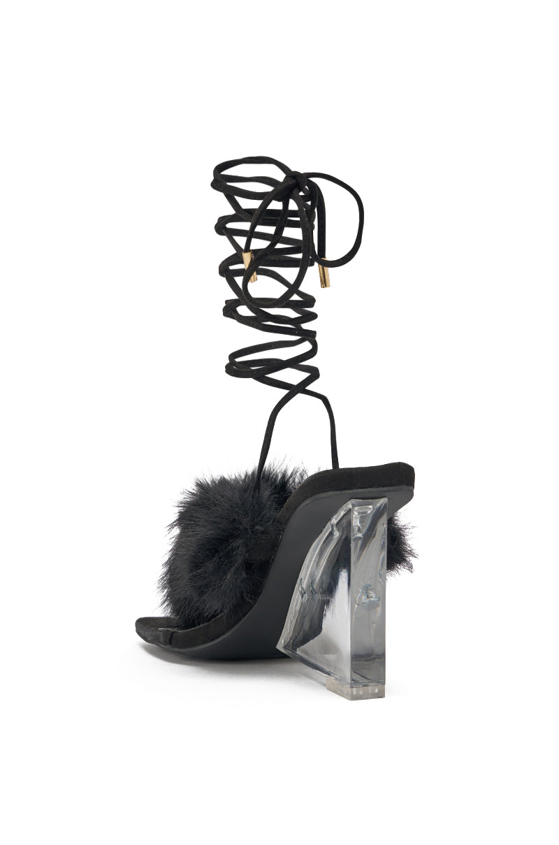 The AKIRA GOLD KIRI BLACK FUR THONG SANDAL WITH CLEAR HEEL is a black faux suede thong sandal with a clear chunky heel, fluffy fur front strap detail, and long black laces for ankle wrap. 5