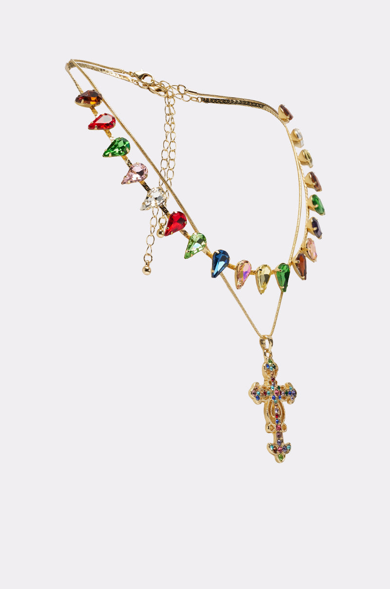 The DOLCE VITA NECKLACE features a gold chain with multicolored, heart-shaped gemstones and a jeweled cross pendant, showcased elegantly on a plain white background. 2