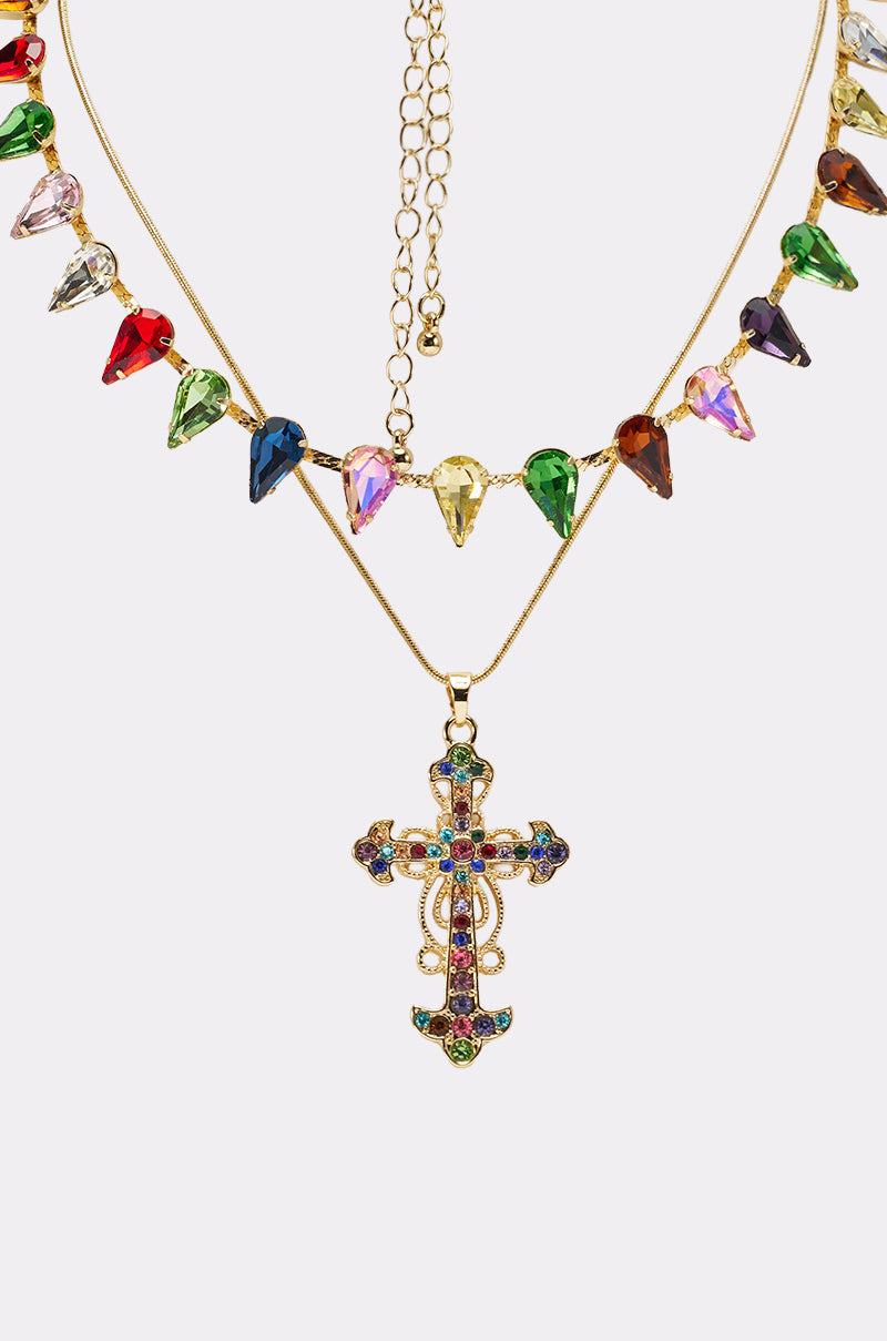 DOLCE VITA NECKLACE: Gold necklace with colorful teardrop gems and a gold cross pendant embellished with multicolored gemstones, showcased on a light background. 3