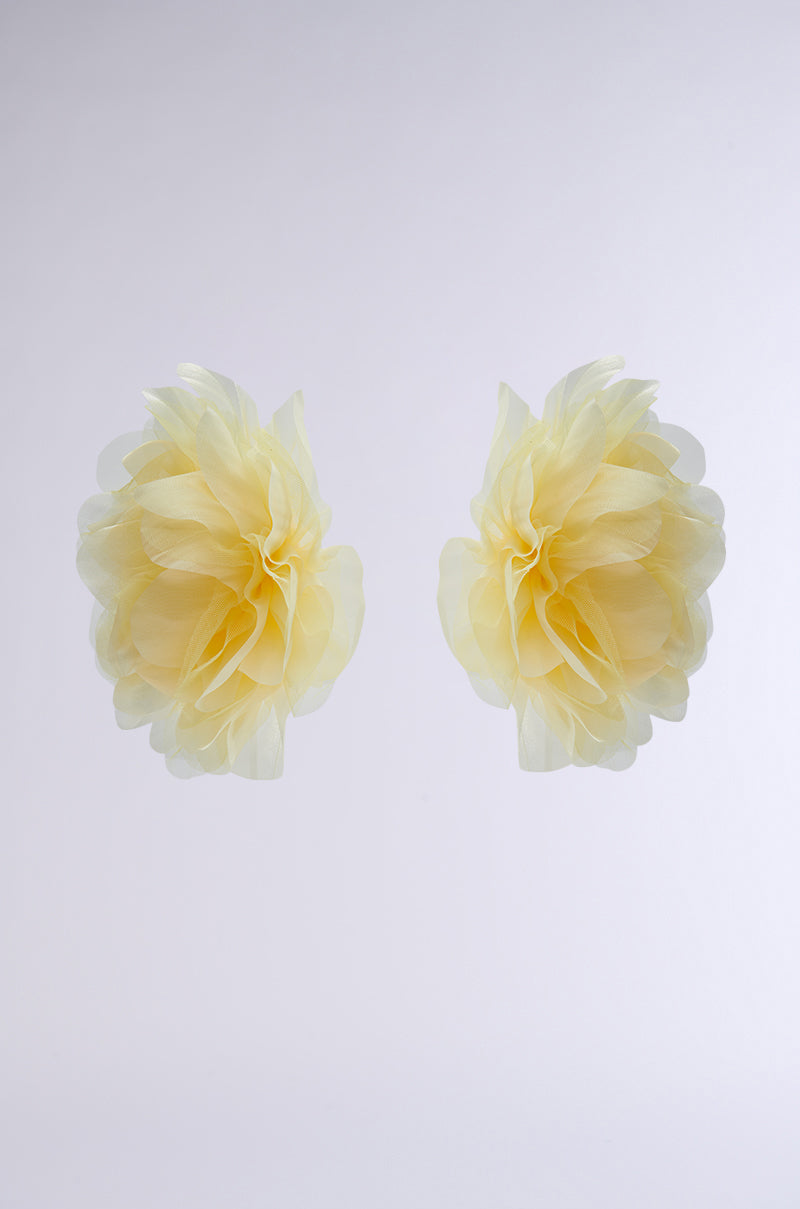 The SO BABY OVERSIZED FLOWER STUD EARRINGS feature two delicate, light yellow tulle flowers with layered petals, arranged symmetrically against a plain white background. 2