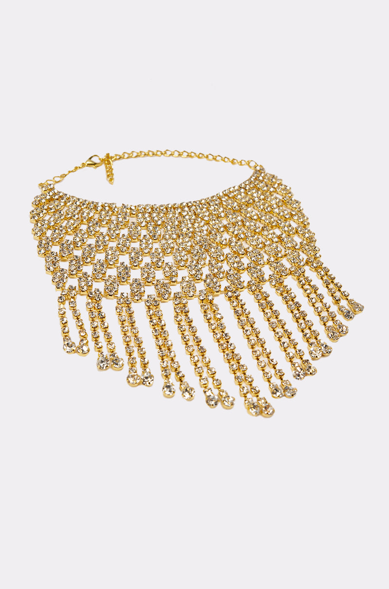 The IN MY ERA BRACELET, a bold rhinestone accessory, pairs perfectly with a gold choker necklace featuring multiple rows of sparkling rhinestones and cascading chain fringe for a glamorous statement against a white background. 2