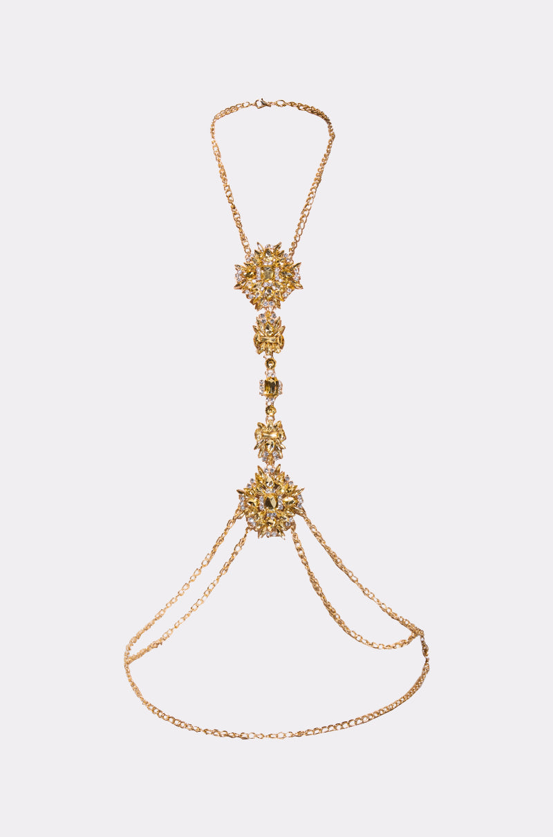 The RIGHT IN BETWEEN BODY CHAIN features a gold-tone design with intricate floral patterns, connecting chains, and rhinestone accents at the center and sides, showcased against a plain white background.