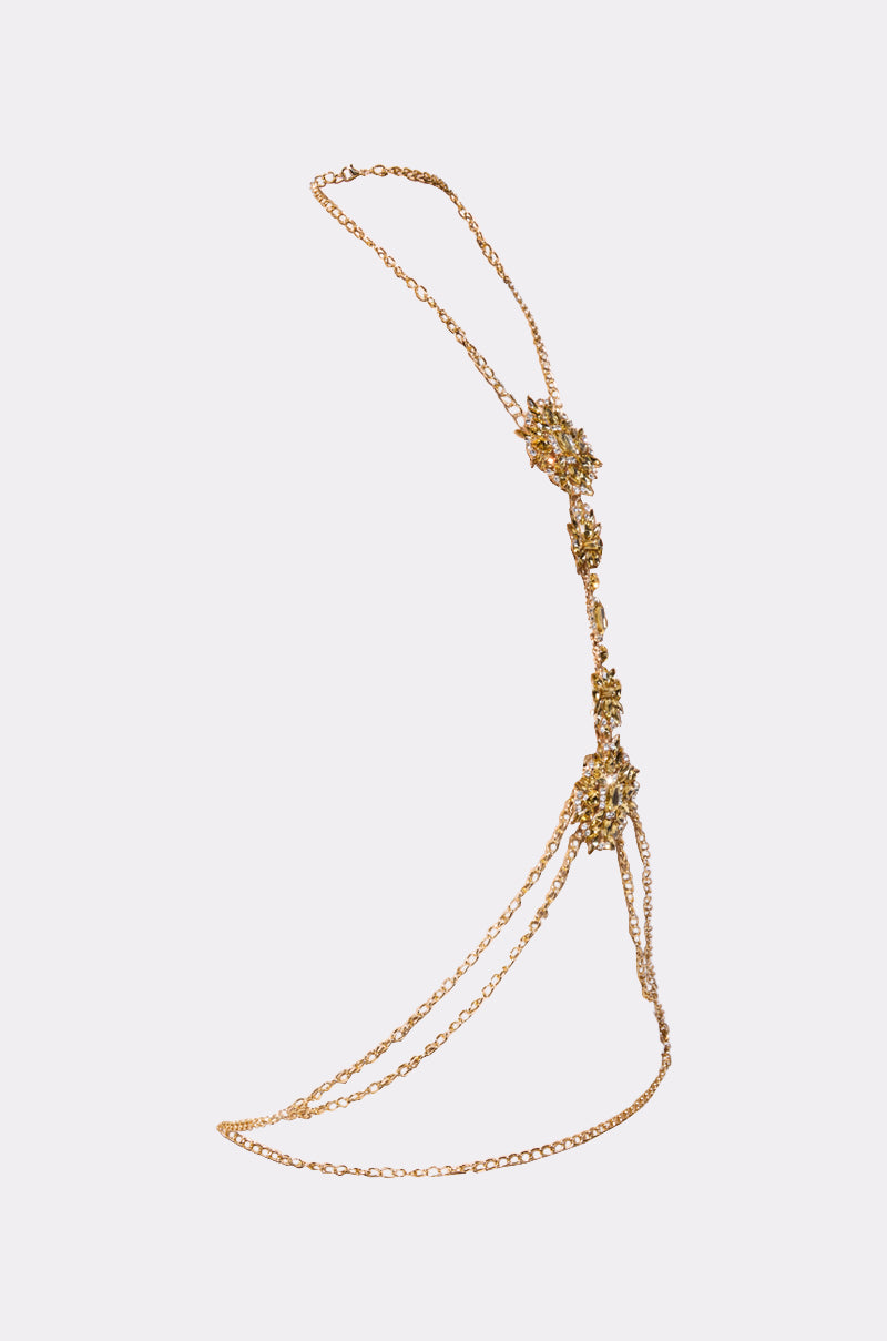 The RIGHT IN BETWEEN BODY CHAIN is a gold rhinestone body accessory with intricate floral clustered details at three points, elegantly draping around the shoulder and waist. Shown against a plain light background, it's a true statement piece.