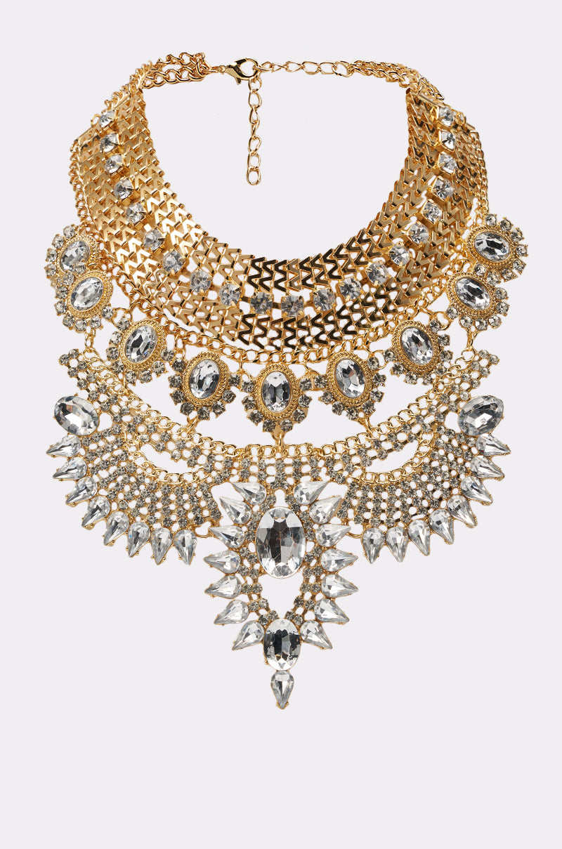The NOSTALGIA NECKLACE features gold layered chains with bold central and hanging oval and teardrop-shaped clear crystals—an intricately detailed statement piece ideal for evening wear. 2