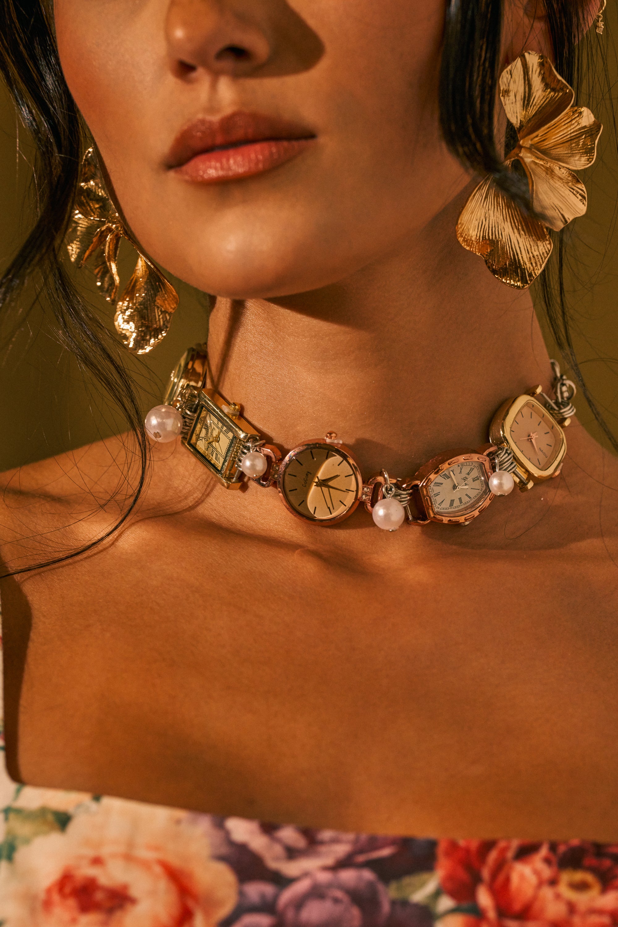 A woman wears gold floral earrings and the WHAT TIME IS IT CHOKER NECKLACE, adorned with vintage watch faces and pearls, paired with a floral off-shoulder top.