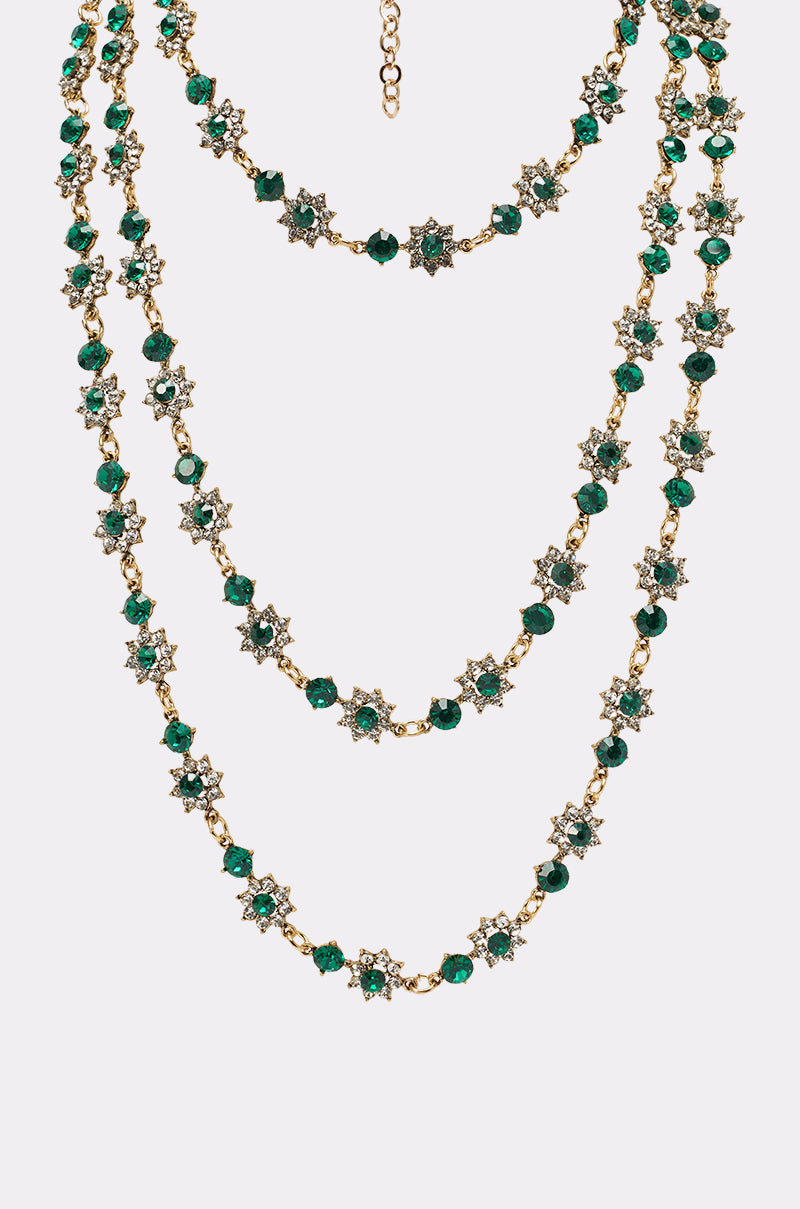 The GOOD FOR IT NECKLACE features three gold-tone layers with emerald green crystal beads and star-shaped floral motifs set with clear crystals, making a stunning statement piece shown on a plain white background. 3