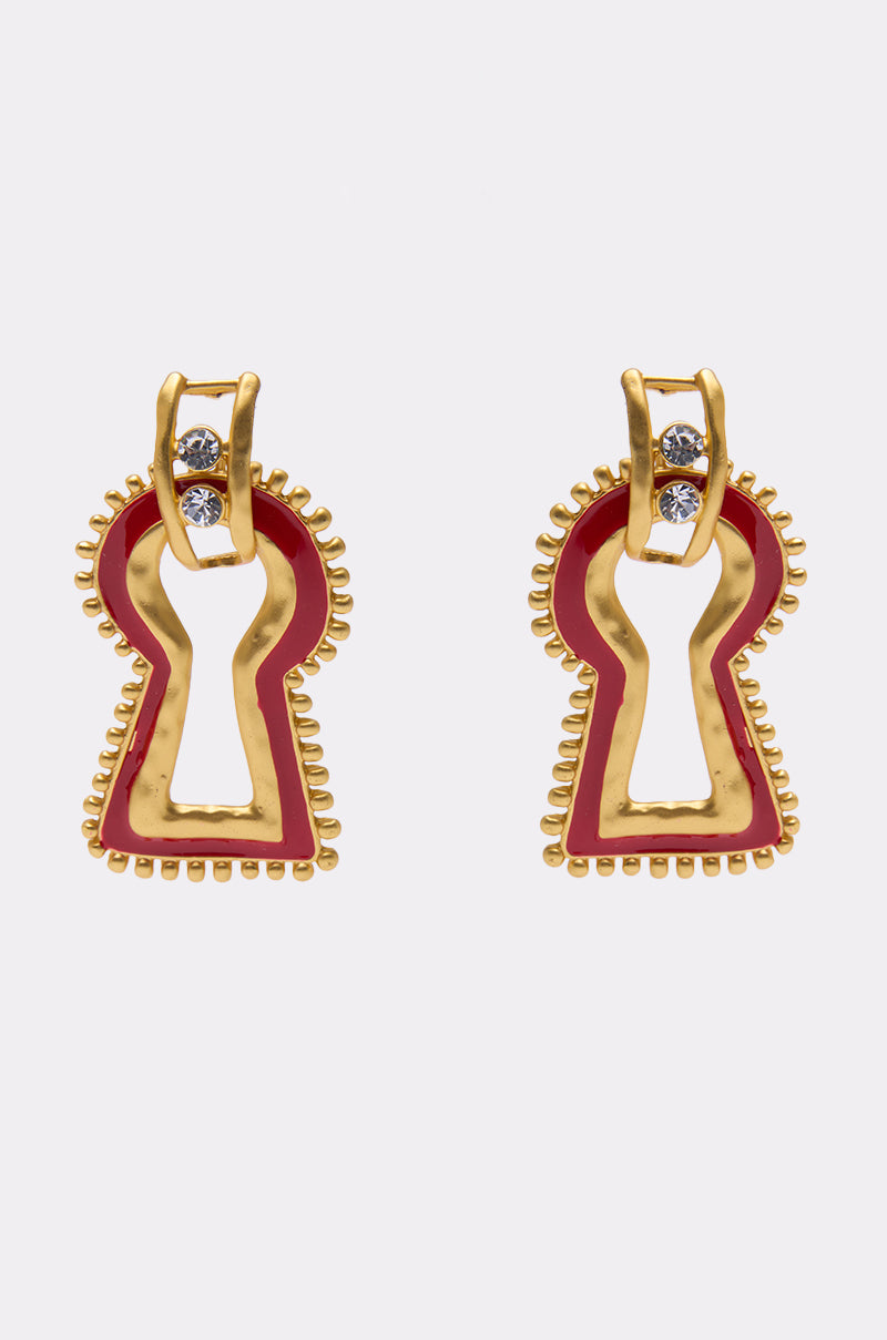 The UNLOCK ME EARRING features gold metallic keyhole shapes with beaded edges, a small top loop, and two clear gemstones on each piece, shown against a plain white background. 1