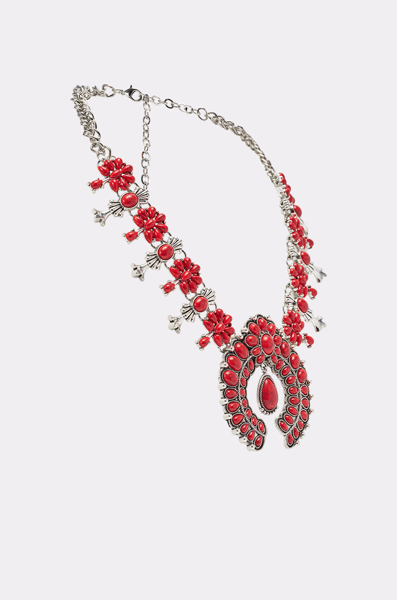The TAKE ME OUT STONE NECKLACE is a western-inspired silver chain with intricate red beaded floral designs and a bold red stone floral pendant, set against a white background. 2