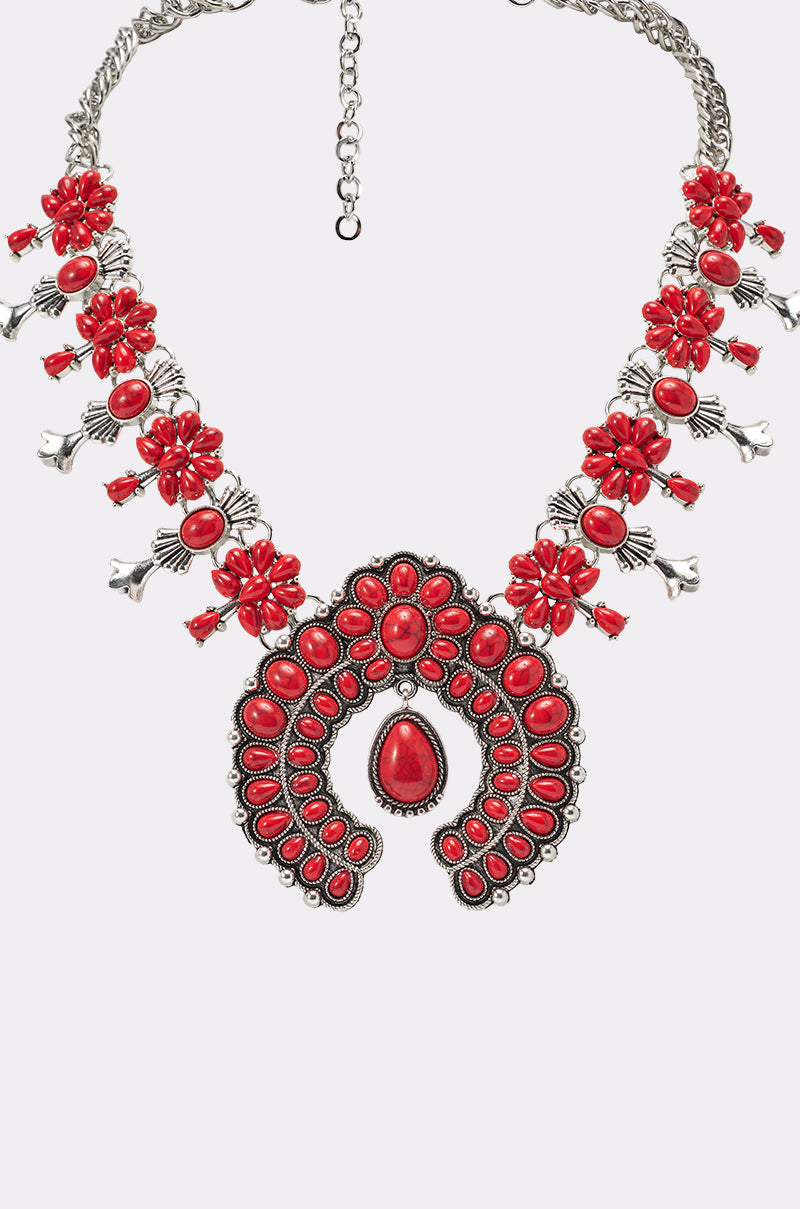 The TAKE ME OUT STONE NECKLACE is a silver statement piece with intricate western-inspired metalwork, vibrant red floral pendants, and teardrop-shaped stones. 3