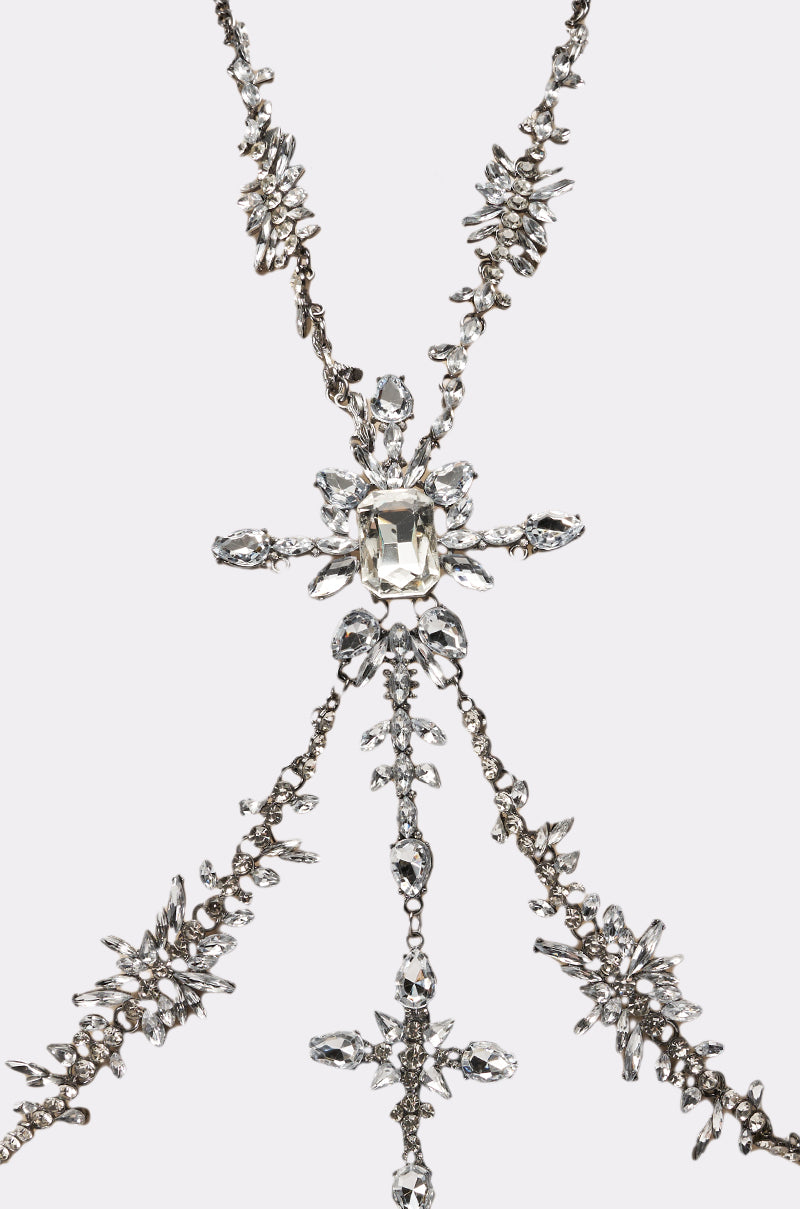 The LUXE ISNT CHEAP BODY CHAIN features intricate crystal chains, sparkling clear gemstones, and a bold central square-cut gem, elegantly displayed against a plain white background. 5