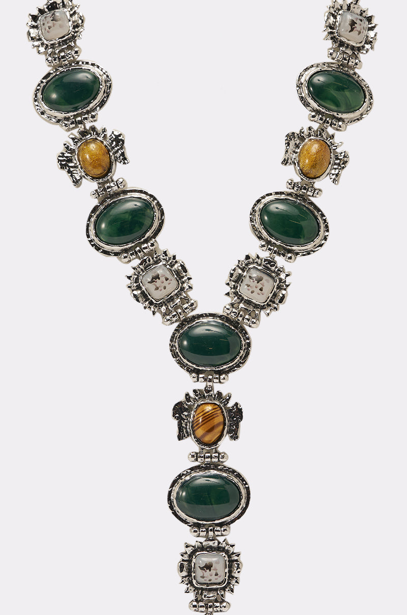 The IM OUTSIDE NECKLACE is a vintage-inspired statement piece with alternating oval green, round yellow-brown, and square clear stones in ornate silver settings, creating a bold V-shape. 3