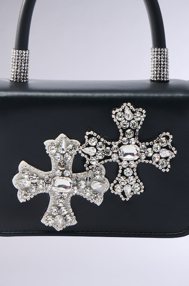 The EVERYTHING CHROME PATCH PURSE is a black handbag featuring two jeweled cross details and rhinestone accents on the handle, designed for chic crossbody wear.