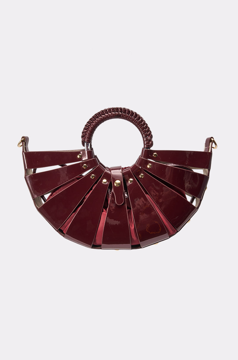 Introducing the CRAZY IN LOVE BAG: a glossy, semi-circular handbag crafted from luxurious burgundy faux leather with gold hardware. This standout accessory features wide, fan-like segmented panels reminiscent of a cage-style crescent bag and is finished with a woven round handle for added elegance.