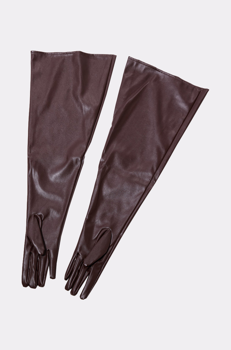 The TAKE IT THERE GLOVES are long, dark chocolate faux leather opera-style gloves with a glossy finish. Laid flat on a light gray background, they extend past the elbows and feature a smooth, fitted look. 4
