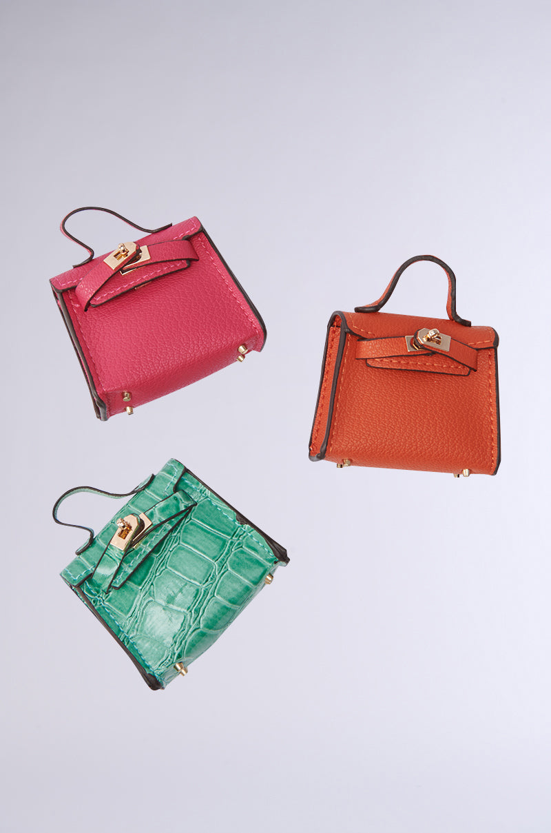 The STAY IN MY BAG HAIR CLIP SET features three small faux leather handbag clips with gold clasps in pink, orange, and green crocodile texture, displayed diagonally against a light gray backdrop.