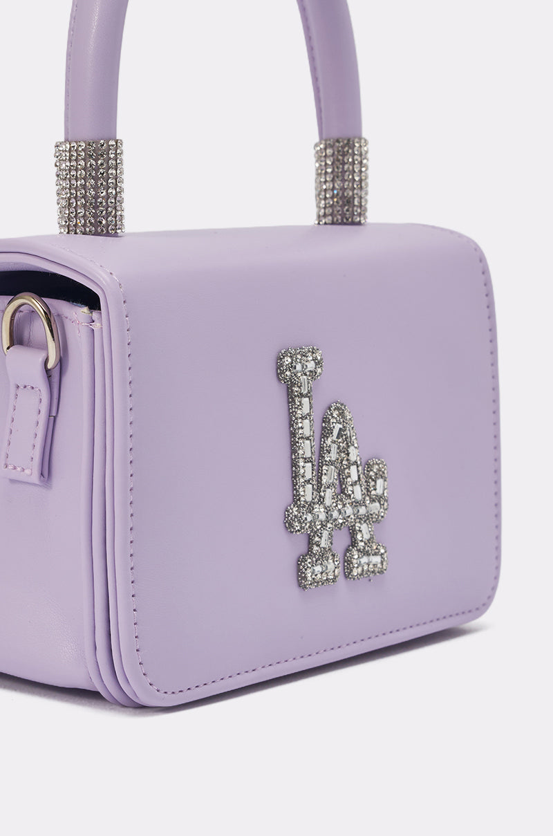 The IN THE CITY APPLIQUE PURSE is a lavender mini handbag adorned with a rhinestone "LA" logo and sparkling rhinestone handle accents—perfect for adding chic, glamorous style to any outfit. 3